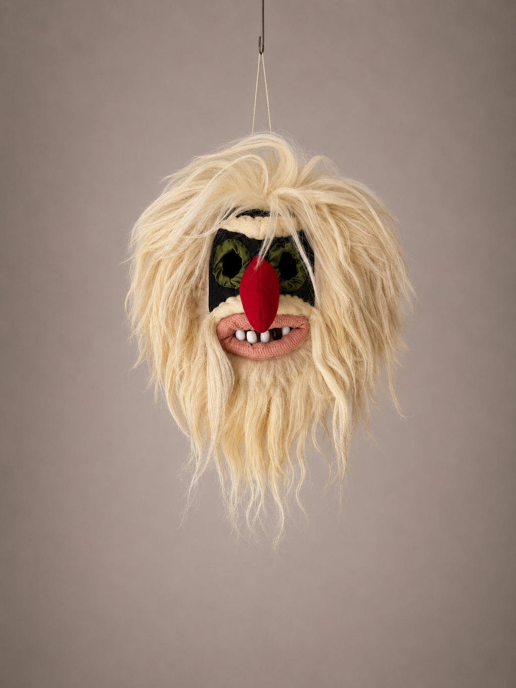 Fuzzy mask with blonde hair, red nose, and black eyes on a plain background