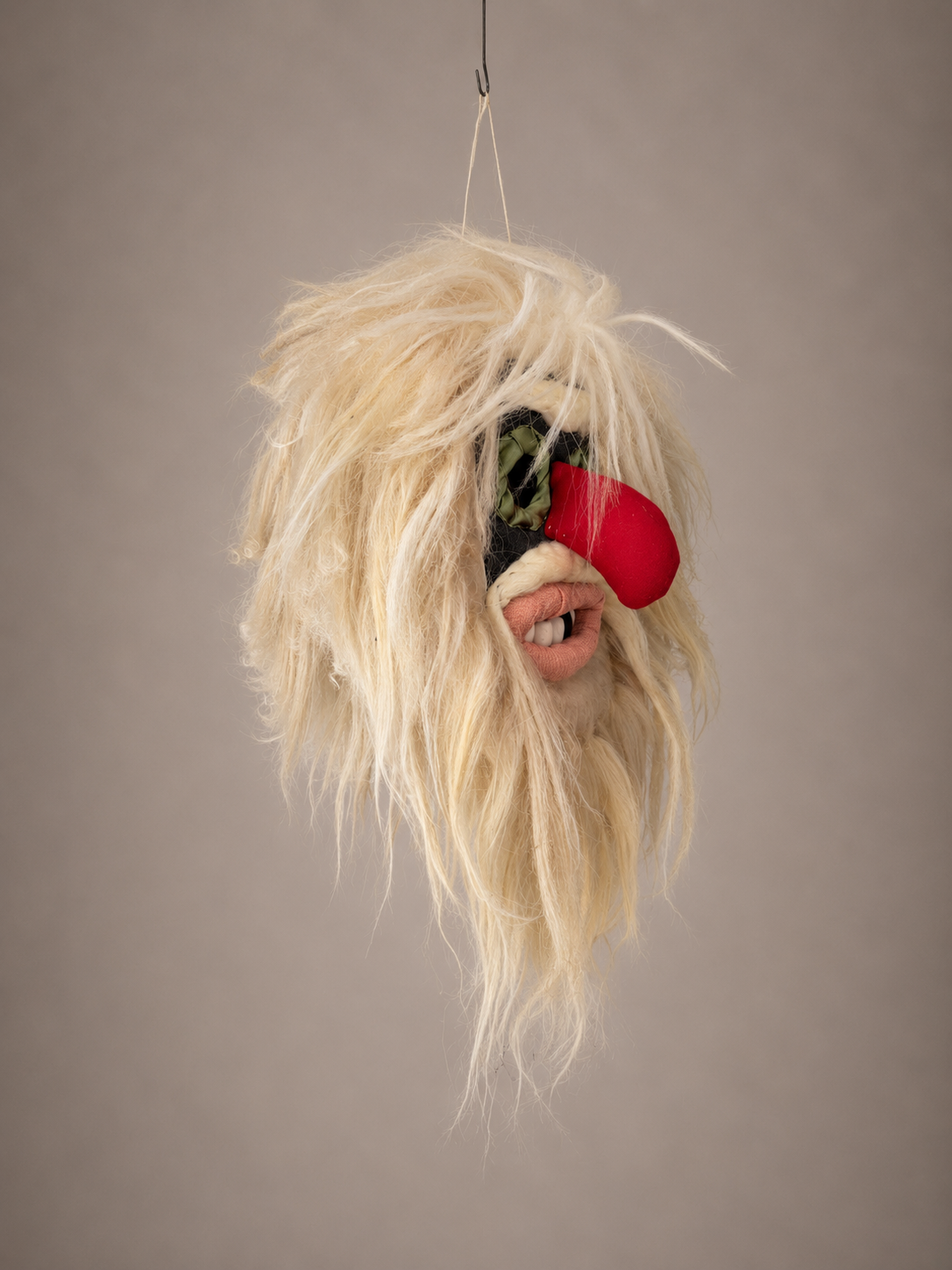 Fuzzy mask with blonde hair, red nose, and black eyes on a plain background