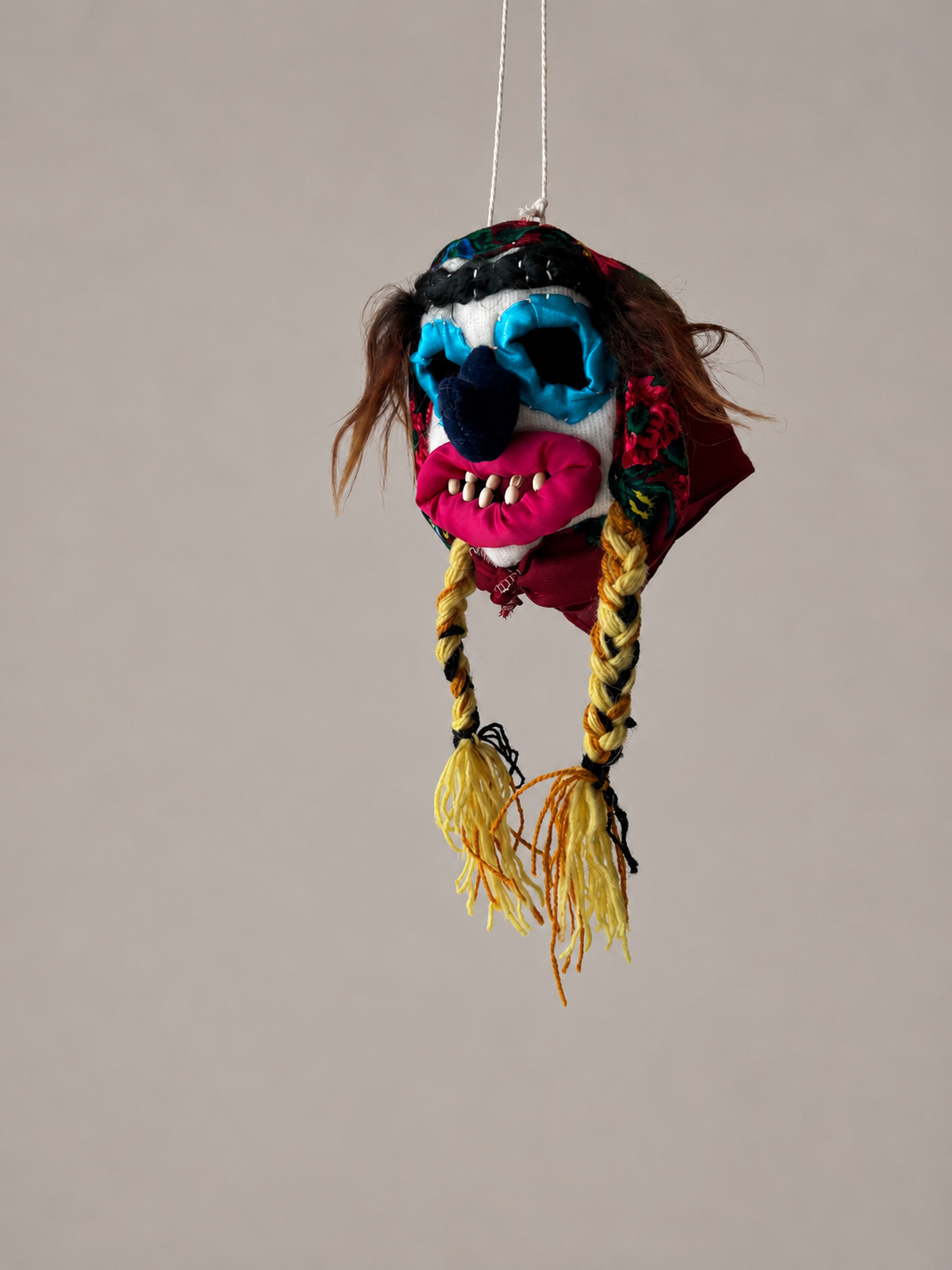Colorful Handmade Mini Mask Baba Folk with braided hair hanging against a plain background