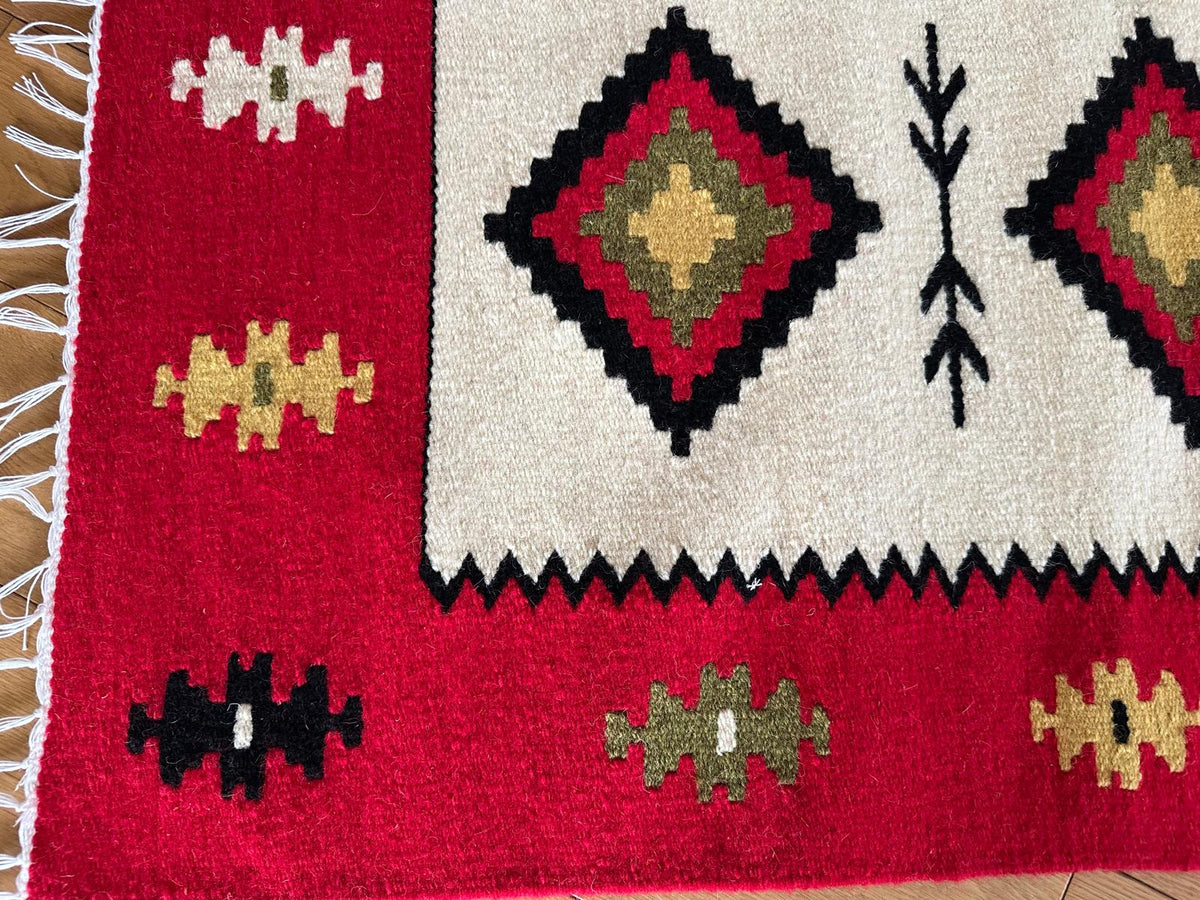 Red and white patterned rug with geometric designs on a wooden floor.