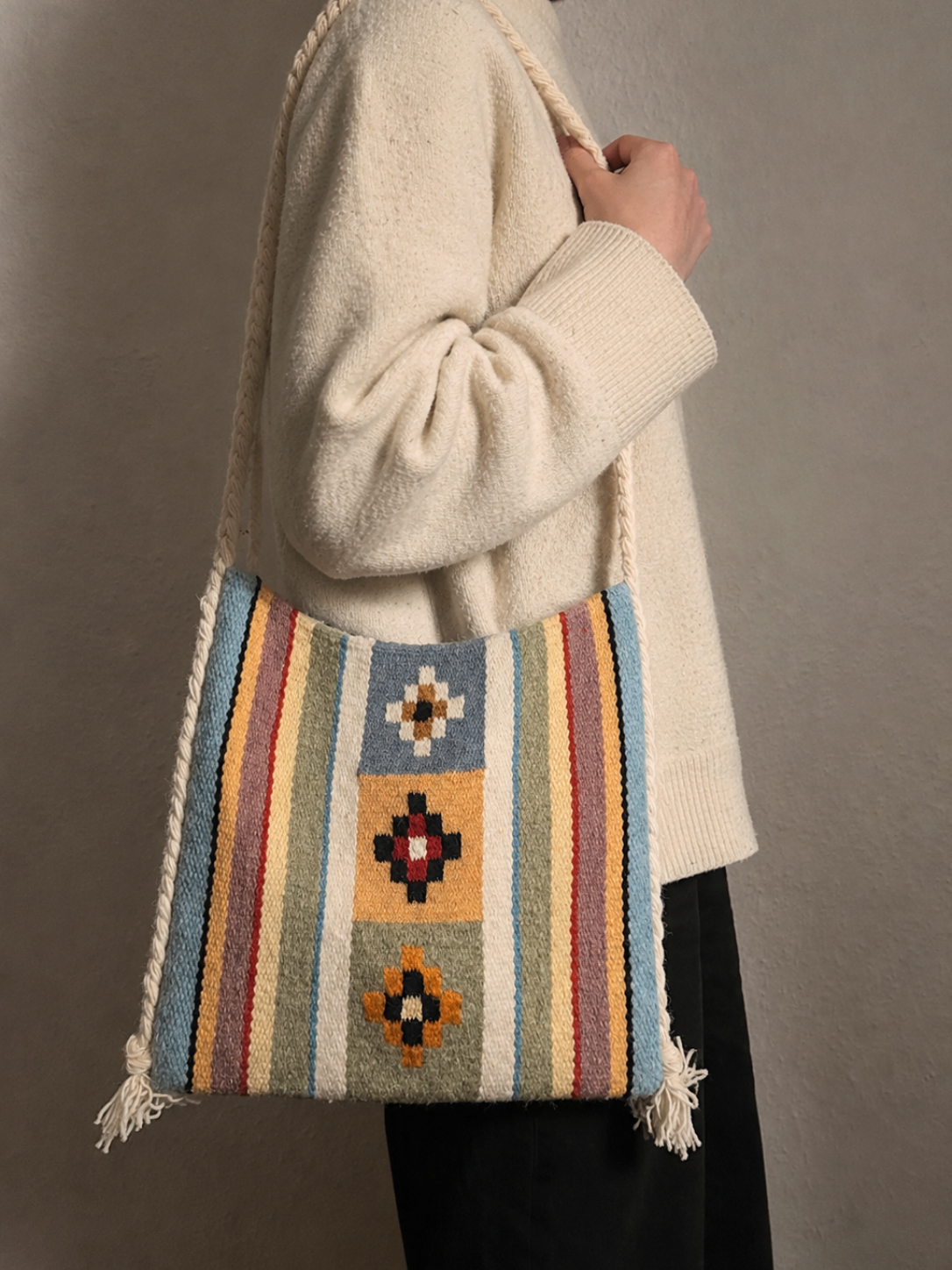 Person holding a colorful woven bag with geometric patterns against a neutral background