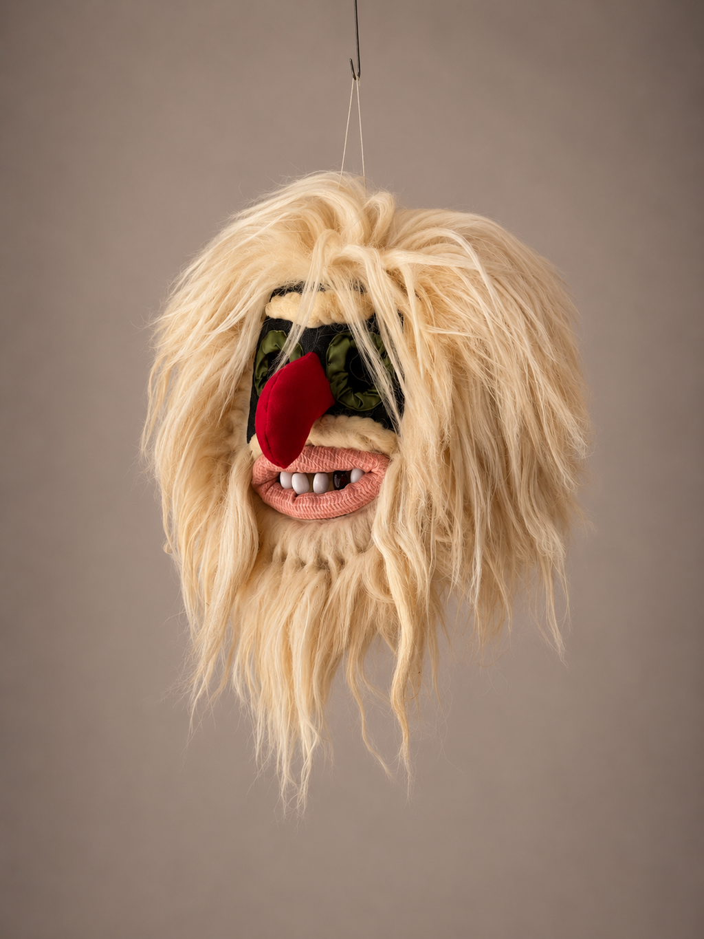 Fuzzy mask with blonde hair, red nose, and black eyes on a plain background
